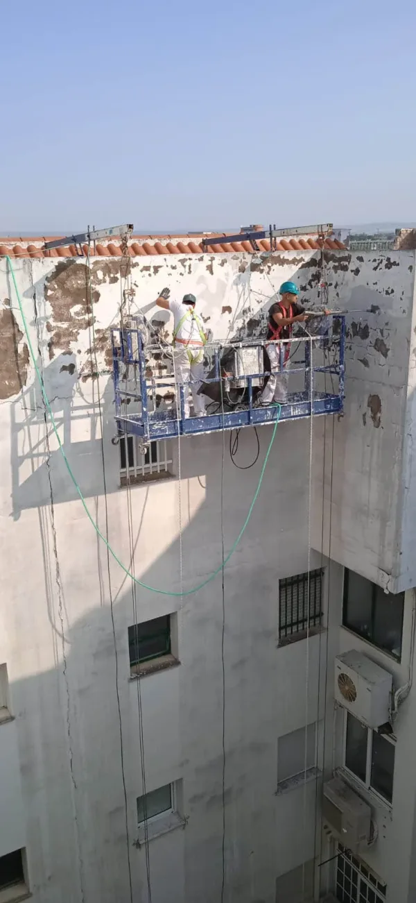 Trabajadores realizando rehabilitación y pintura en patio interior de edificio en Sevilla, con sistemas de seguridad vertical